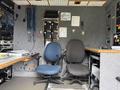 Interior of a vehicle featuring two office chairs facing a control panel with various equipment and wiring