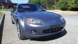 A 2007 Mazda Miata in grey with a sleek design featuring round headlights and a prominent grille showcasing its sporty character