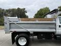A 2004 Ford F-750 dump truck with a large silver dump bed and a side-mounted lever for unloading materials