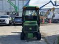 A 2021 John Deere 1575 lawn mower with a green exterior and enclosed cabin positioned in front of a fence and construction equipment