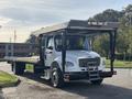 A 2022 Freightliner M2 106 flatbed truck with a white cabin and a silver flatbed is parked at an angle showcasing its front and side features