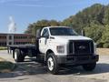 A 2018 Ford F-750 truck with a white exterior and a flatbed design parked on a street with a black grille and orange rooftop lights