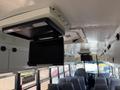 Interior view of a school bus featuring two mounted screens on the ceiling and rows of gray passenger seats visible below