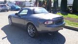 A 2007 Mazda Miata in gray with a retractable hardtop and sporty alloy wheels viewed from the rear angle