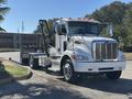 A white 2020 Peterbilt 330 truck with a silver grille and orange lights on top is positioned at an angle, showcasing its front and side profile with an attached flatbed dolly