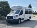 A 2018 Ford Transit-350 shuttle bus with a white exterior and large side windows parked on a concrete surface