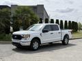 A white 2021 Ford F-150 pickup truck with four doors and a cargo bed parked on a concrete surface