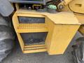 A yellow storage compartment with textured steps attached to a larger machinery frame, featuring a green cap on top and part of a wheel visible to the side