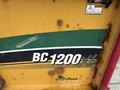 A close-up of a yellow machine with the label BC-1200XL and Smart Feed visible on its body, featuring green accents and some rust on the surface
