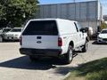 White 2014 Ford F-250 SD with a truck bed cover parked on a lot showing its rear side and chrome wheels
