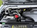 The engine compartment of a 2013 Ford E-350 featuring a battery several fluid reservoirs and various hoses and wires