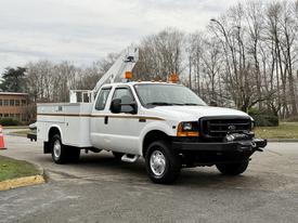 A 2001 Ford F-350 utility truck with a white exterior and an elevated platform on the bed for maintenance work orange lights at the top and a winch on the front