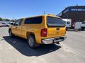 A yellow 2013 Chevrolet Silverado 1500 pickup truck with a cap on the bed parked in a lot showing its rear and side view