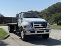A 2008 Ford F-750 flatbed truck with a shiny silver front grill and large tires parked on a road