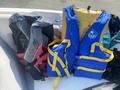 A red and gray life jacket alongside a blue life jacket with yellow straps resting on a boat seat