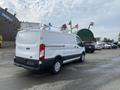 A 2017 Ford Transit van in white color with a cargo area and roof rack visible from the rear angle