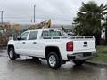 A 2015 GMC Sierra 1500 pickup truck in white with a metal ladder rack on the bed and chrome accents on the rear and wheels