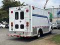 A 1994 GMC Vandura 3500 ambulance with a white body and blue stripe displaying red taillights and emergency lights on the back