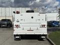 A white 2024 Ford F-550 truck with a boxy cargo area and a spare tire mounted on top is seen from the rear