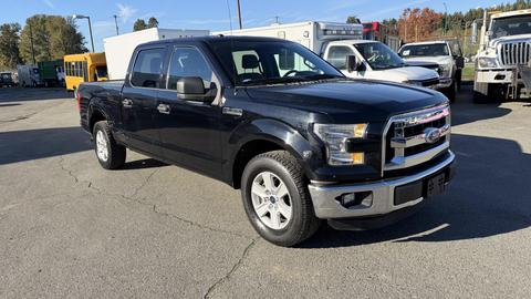A 2016 Ford F-150 in black with a double cab and chrome accents parked on a lot with various vehicles in the background