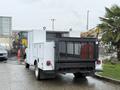 A 2000 Ford F-450 with a utility body featuring a black mesh tailgate and multiple lights on top parked in a lot