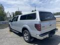 A silver 2014 Ford F-150 truck with a camper shell and off-road tires parked on gravel