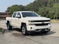 A white 2017 Chevrolet Silverado 1500 with chrome accents parked with its front facing the viewer showcasing its large grille and modern design features