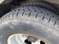 A close-up of a treaded tire mounted on a steel wheel with visible lug nuts and branding on the sidewall