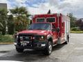 A red 2007 Ford F-550 ambulance with a front-mounted winch and lights on top parked on a paved area