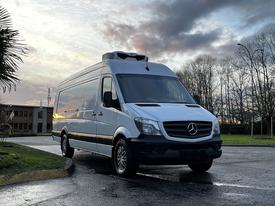 A 2018 Mercedes-Benz Sprinter van in white with a tall roof and black trim parked on a road
