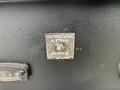 A metal control panel with a labeled button for "OUTRIGGERS & TOOLS" and the word "DERRICK" on a textured black surface