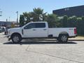 A 2023 Ford F-350 SD in white with a spacious crew cab and four-wheel drive logo on the side parked on a concrete surface
