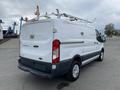 A white 2017 Ford Transit van with a roof rack and rear doors partially open