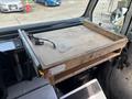 A wooden flat work surface attached to a vehicle's interior with a power cord visible on the side