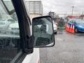A 2008 Suzuki Carry with a side mirror reflecting rain droplets and a blurred view of vehicles in the background