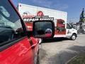 A red 2013 RAM 2500 truck with a side mirror focused on the foreground showing a reflection of a delivery truck in the background