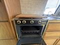A 1976 GMC Motorhome kitchen stove and oven with four knobs and an open oven door displaying a rack inside