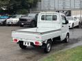 A white 2010 Suzuki Carry small truck with an open cargo bed and a compact cab design parked in a lot