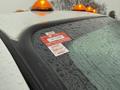 A 2015 Ford F-450 with orange warning lights on the roof showing rain on its surface and a certificate of approval sticker on the window