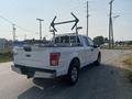 A white 2016 Ford F-150 with a metal rack mounted in the truck bed parked on a gravel roadside