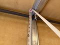 A measuring tape is extended along a metal beam in a garage setting with the numbers clearly visible on the tape showing measurements