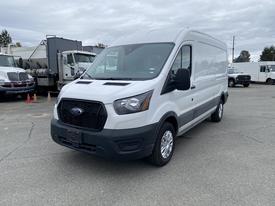 A 2024 Ford Transit van with a white exterior and gray accents, featuring a black grille, front headlights, and silver wheels positioned in a parking lot