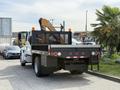 A 2011 International 4300 flatbed truck with a yellow crane attachment on the rear and a black mesh guard surrounding the cargo area