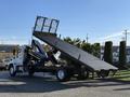 A white 2015 Hino 358 flatbed truck with a raised ramp and hydraulic lift arms extended for loading and unloading cargo