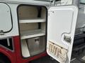 A white and red utility cabinet door open to reveal two shelves and a metal compartment inside along with a pouch holding tools or accessories