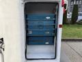 A white utility truck with an open compartment displaying four blue storage boxes stacked inside