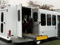 A white 2017 Ford E450 with an open door and a wheelchair lift extended, showcasing accessibility features for passengers with mobility needs
