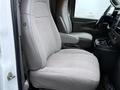 A gray upholstered front seat of a 2016 GMC Savana van with an adjustable armrest and cup holders in the console