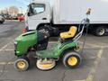 A 2021 John Deere L Series S lawn mower with a green body yellow seat and a circular cutting deck positioned in a parking lot