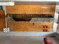 A wooden storage box mounted on a wall with metal edges and a single lock attached, accompanied by three red tools and an electrical outlet nearby